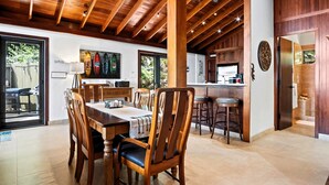 Un comedor amplio con sillas de madera y una mesa grande, una cocina con armarios de madera, y un techo con vigas a la vista.