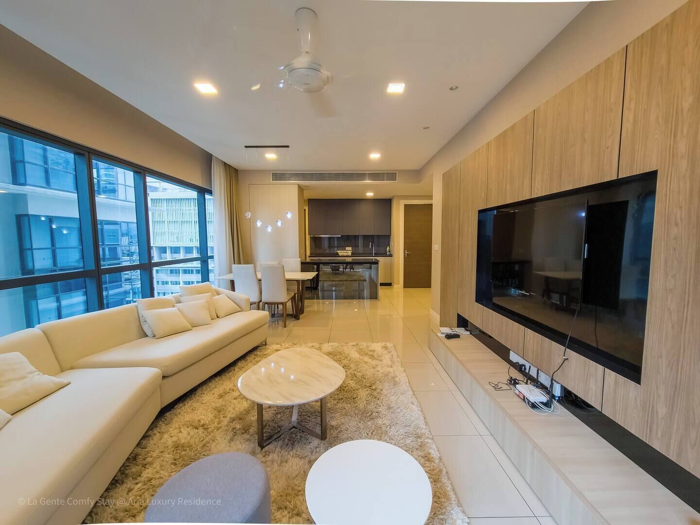 Ein modernes Wohnzimmer mit einer Couch, zwei Couchtischen, einem Fernseher und einer Küche im Hintergrund.