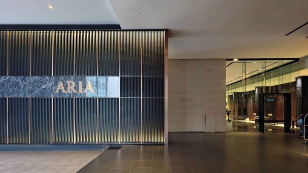 Un vestíbulo moderno con un gran letrero 'ARIA', un espacio amplio con piso de baldosas y una entrada de vidrio que da a una zona de estar.