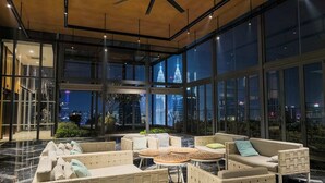 Un espacio interior amplio con techos altos, ventanas grandes y vistas de edificios urbanos de noche.
