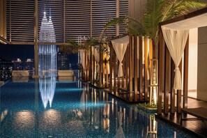 Piscina interior moderna con vista al horizonte de la ciudad, rodeada de estructuras de madera y palmeras.