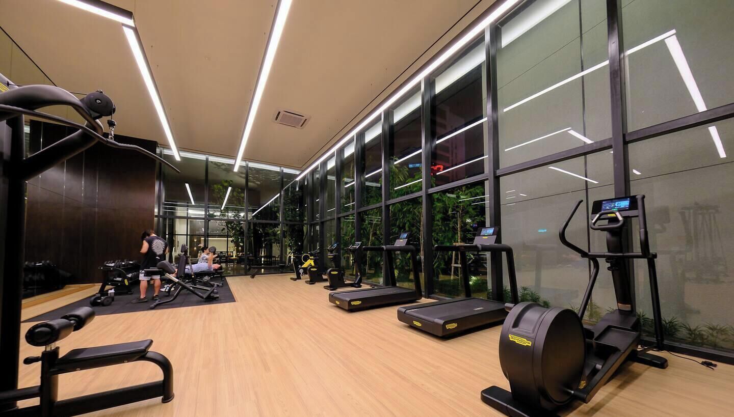 Et moderne fitnesscenter med løbebånd, styrketræningsudstyr og store vinduer med udsigt til grønne områder.