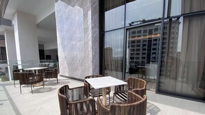 Ein moderner Außenbereich mit Korbstühlen, einem Tisch, großen Fenstern und Blick auf die Stadtlandschaft.