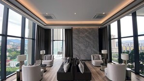 Ein modernes Wohnzimmer mit einer schwarzen Couch, zwei Sesseln und einem Couchtisch. Große Fenster bieten Blick auf die Stadt.