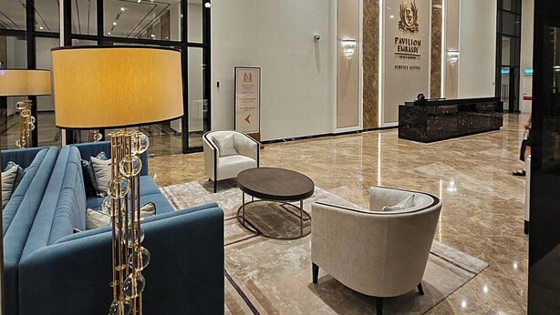 A modern lobby with a blue sofa, a lamp, and a decorative floor lamp. There is a sign for Pavilion Embassy Service Suites. - 2BR Luxury Living KLCC 600mbps (Kuala Lumpur)