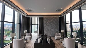 A modern living room with a black sofa, two armchairs, and a coffee table. Large windows offer a city view.
