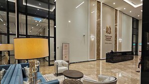A modern lobby with a blue sofa, a lamp, and a decorative floor lamp. There is a sign for Pavilion Embassy Service Suites.