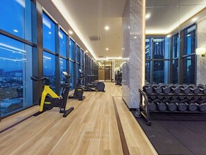 Un gimnasio con equipamiento de ejercicio, amplias ventanas y vistas a la ciudad.