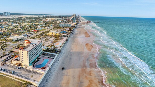 Vista aérea de un hotel costero con playa, piscina y aparcamiento.