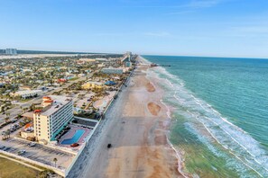 An aerial view of a coastal hotel with a beachfront, a swimming pool, and a parking lot. - Modern Beach Oasis 
Sleeps 4~Pool~Gym~Kitchen~Games~Parking (Daytona Beach)