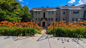 A multi-story residential building with a central entrance, surrounded by a garden with orange flowers. - Chic Stratton Condo- Walking Distance to Village (Stratton)