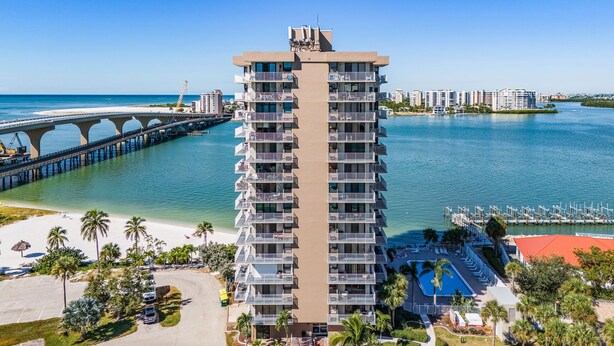 Ein Hochhotel mit mehreren Balkonen, Blick auf den Strand und einer Marina mit Booten.