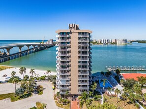 Un hôtel de grande hauteur doté de nombreux balcons, offrant une vue sur la plage et donnant sur une marina où sont amarrés des bateaux.