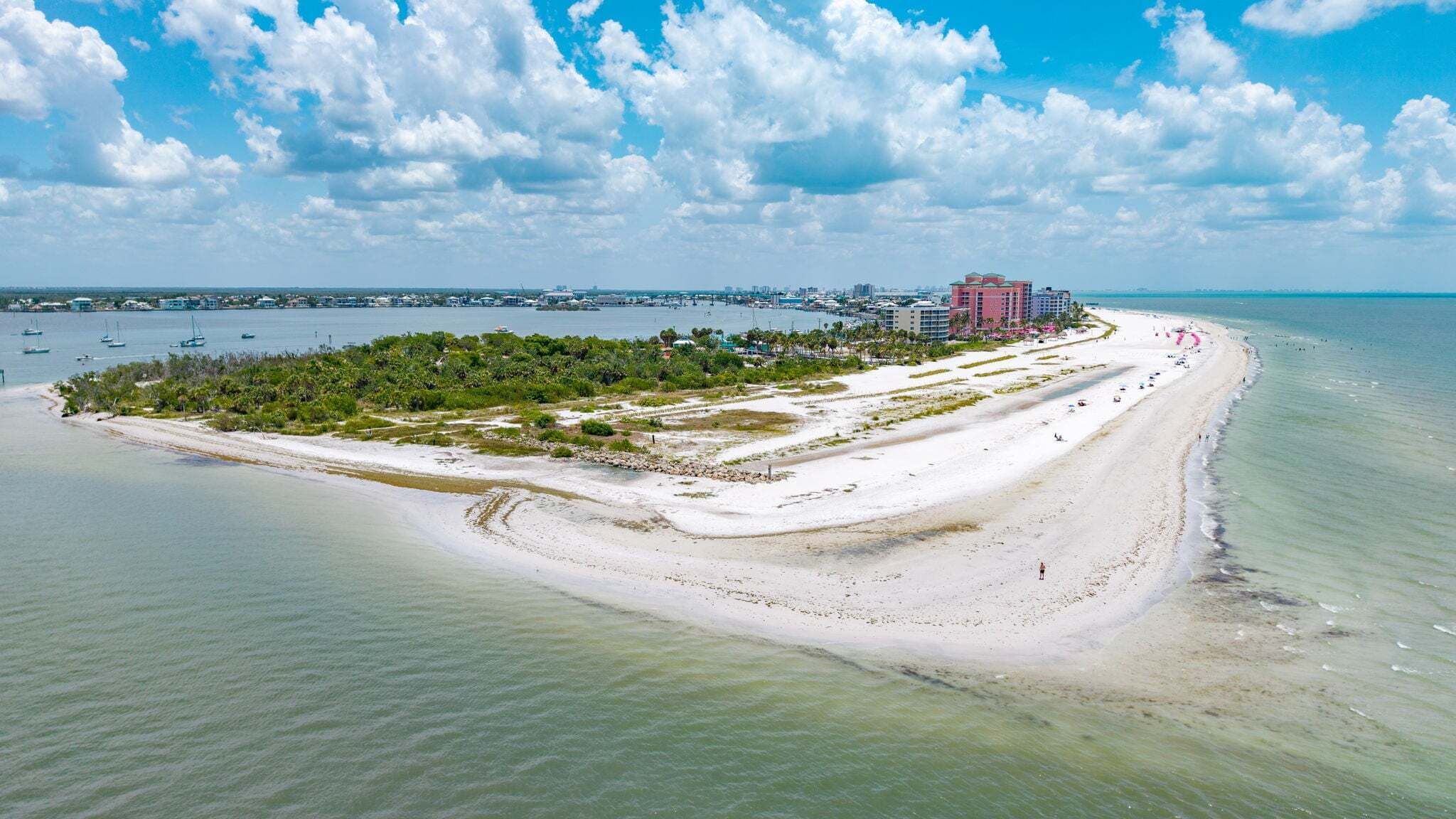 Un complejo turístico costero con playa de arena, un puerto deportivo y un hotel de fachada roja.