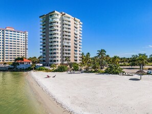 A beachfront hotel with multiple floors, a sandy beach, and palm trees. - Coastal Bliss with Gulfside Charm — Your Perfect FMB Escape Awaits! – Beach Haven (Fort Myers Beach)