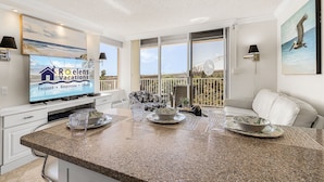 Eine moderne Küche mit einer Granit-Arbeitsplatte, eine Essecke mit einem weißen Sofa und ein großer Fernseher, der 'Roelens Vacations' zeigt.