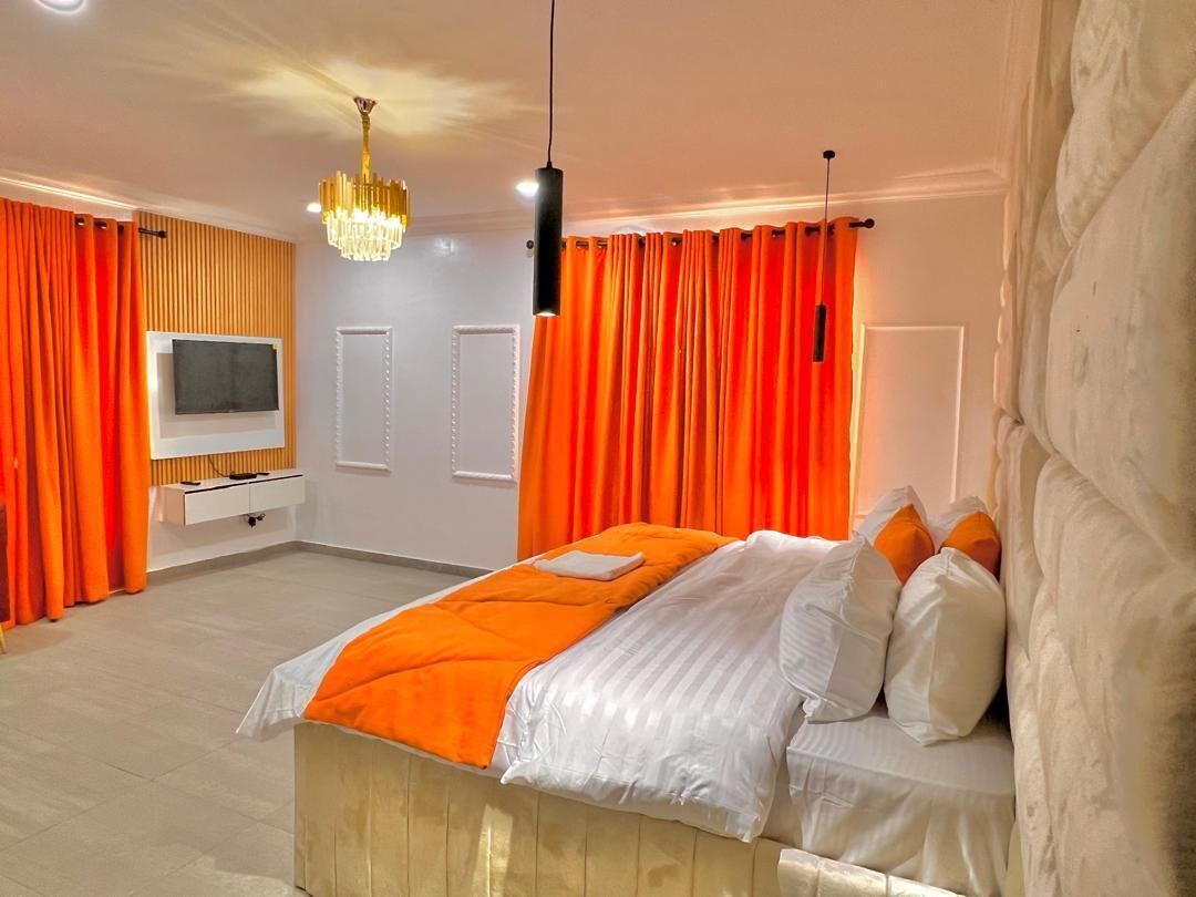 Un dormitorio con cama, cortinas naranjas, televisor y candelabro.