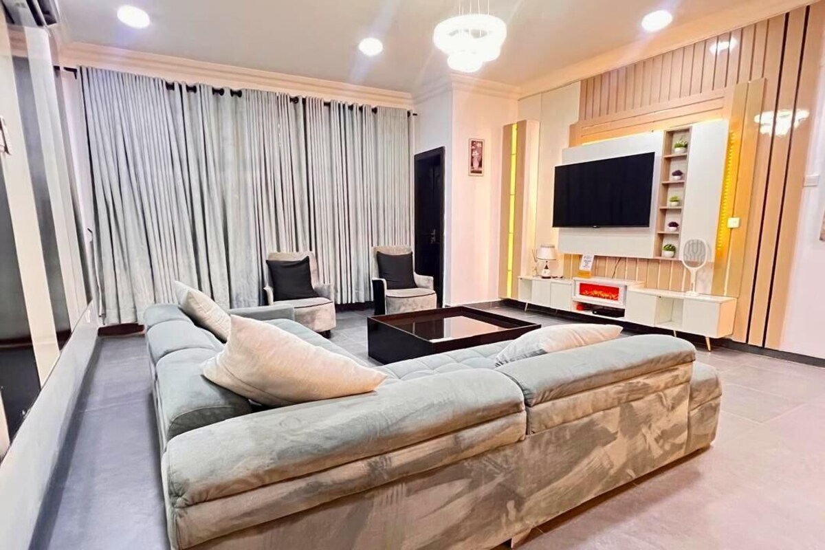 A modern living room with a large sectional sofa, a flat-screen TV mounted on the wall, and a coffee table.