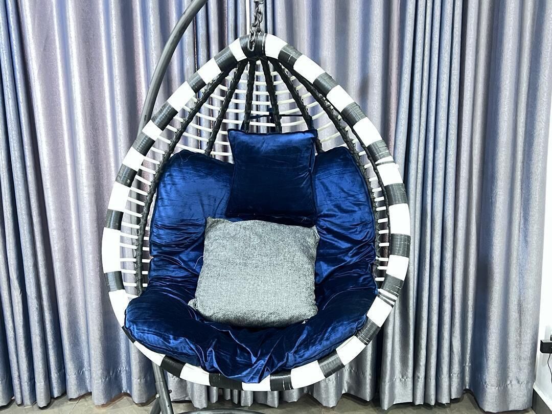 A hanging chair with a blue cushion and a gray pillow, suspended by a black and white rope.