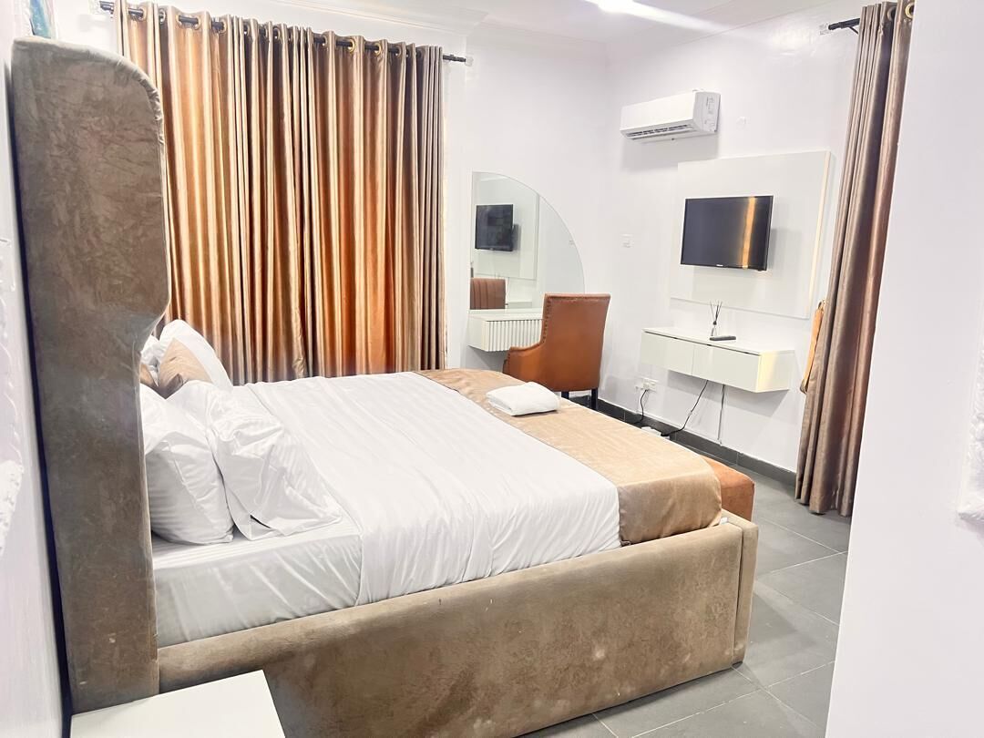 A hotel room with a bed, a desk, a chair, a TV, and a mirror.
