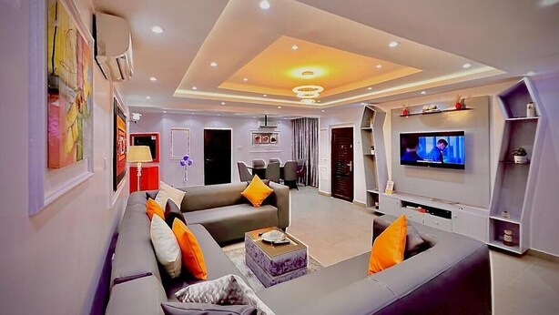 A modern living room with a large sofa, a TV, and a dining area in the background. - The Global Enterprise (Lagos)