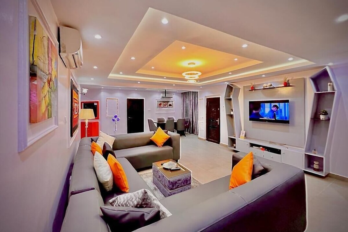 A modern living room with a large sofa, a TV, and a dining area in the background.