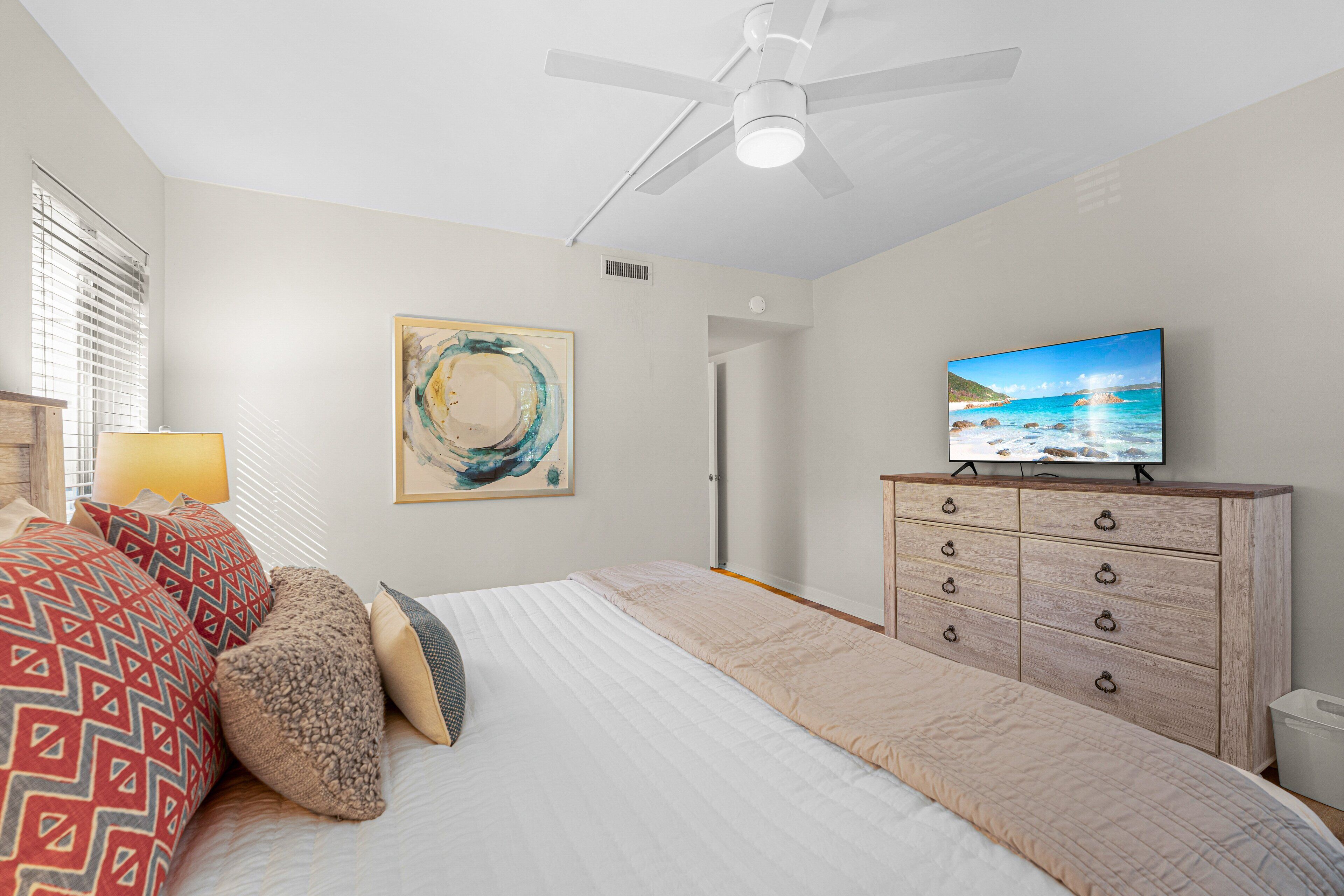 A bedroom with a bed, a dresser, a television, and a ceiling fan.