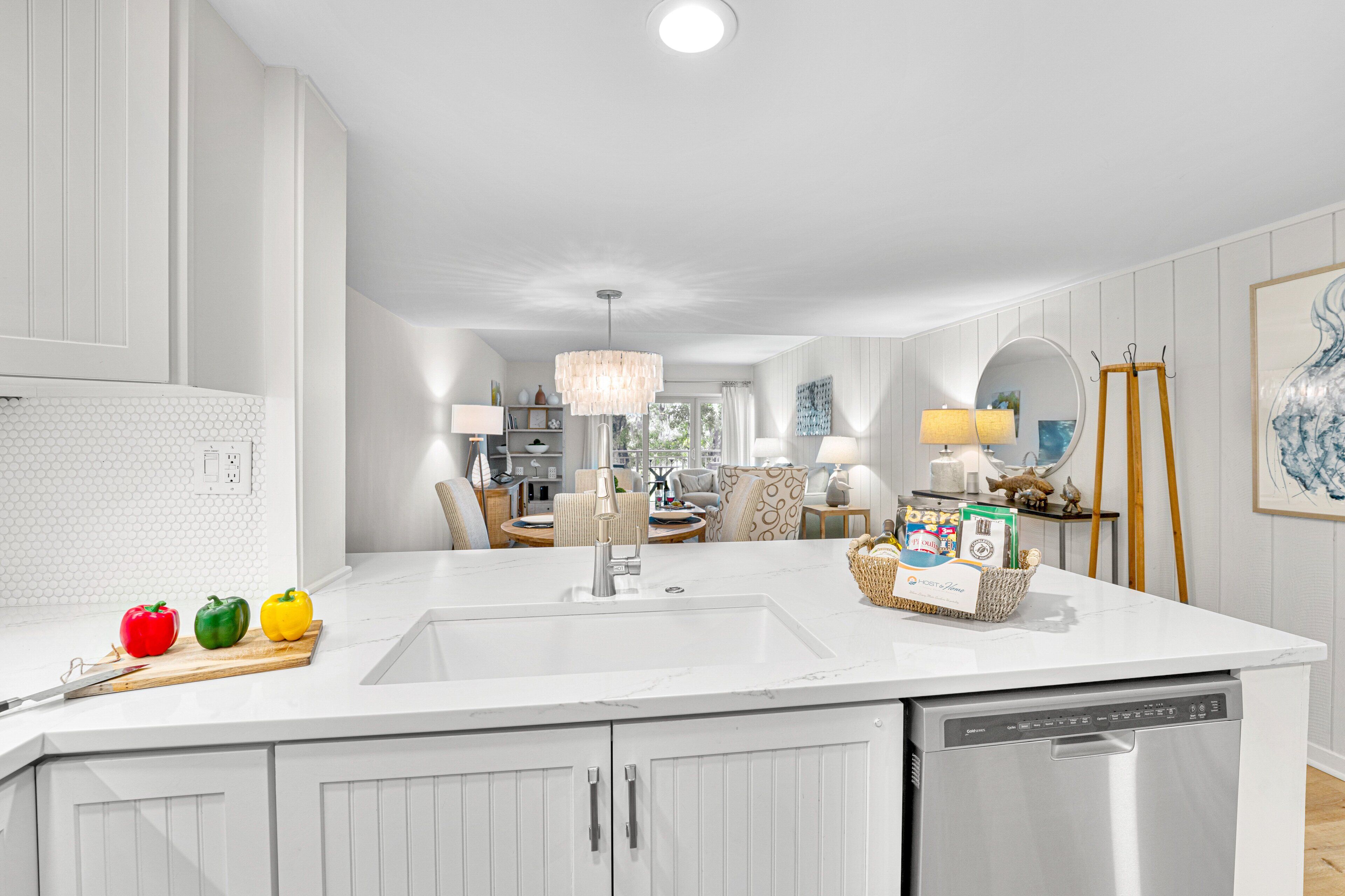 Una cocina moderna con armarios blancos, una isla grande con lavavajillas incorporado y un comedor al fondo.