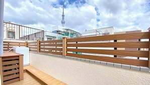 A wooden deck with a railing, a small table, and a white appliance, overlooking a cityscape with a prominent tower. - H401 ＊[New] Tokyo luxury guesthouse｜Japanese style 2DK｜Honjo-Azumabashi station & direct airport access｜Near Asakusa & Skytree (墨田区)