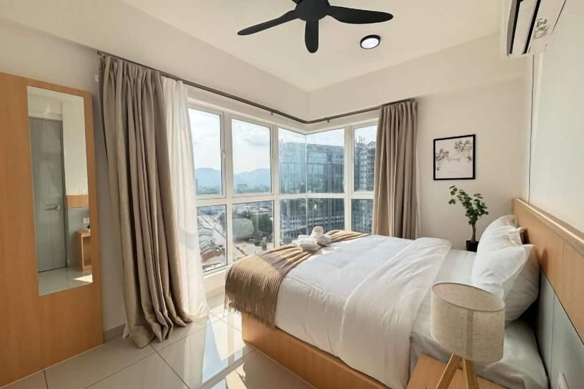Una habitación de hotel moderna con una cama grande, un ventilador de techo, vistas a la ciudad y una ventana con cortinas.