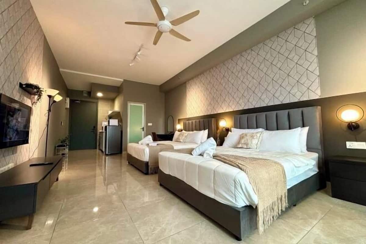 Una habitación de hotel con una cama grande, una cama más pequeña, un televisor, un escritorio y un ventilador de techo.