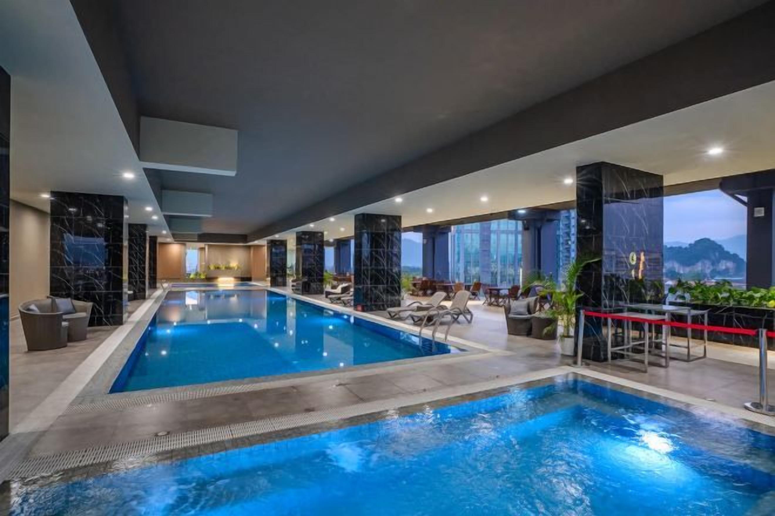 An indoor swimming pool with a view of the mountains, surrounded by lounge chairs and a bar area.