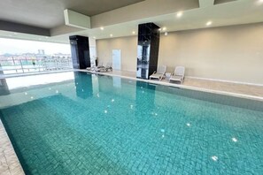 Une piscine intérieure à l’eau claire, entourée de chaises longues et dotée d’un plafond très haut.