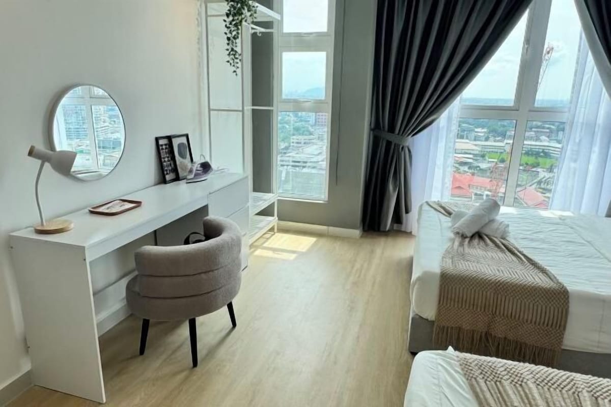 Une chambre moderne équipée d’un bureau, d’une chaise, d’un lit avec une couverture et offrant une vue sur la ville grâce à de grandes fenêtres.