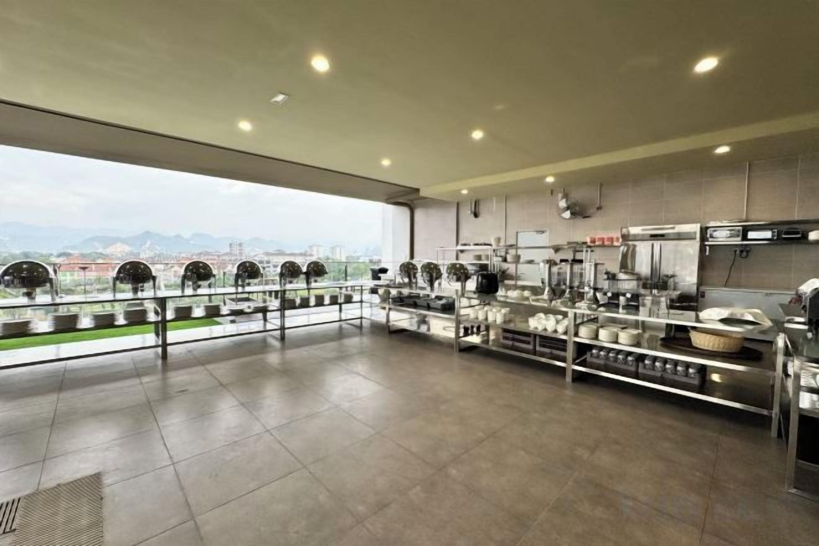 Una cocina comercial espaciosa con electrodomésticos de acero inoxidable, un ventanal con vistas a la ciudad y un techo alto con iluminación empotrada.