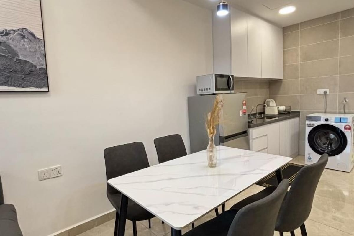 Une cuisine moderne équipée d’un four à micro-ondes, d’une cuisinière et d’un lave-linge. On y trouve une table à manger avec des chaises et un vase contenant des fleurs séchées.