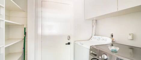 A laundry room with a washing machine, a drying machine, and a mop leaning against the wall.