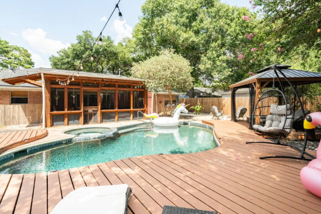 A backyard with a wooden deck, a hot tub, and a swing chair.