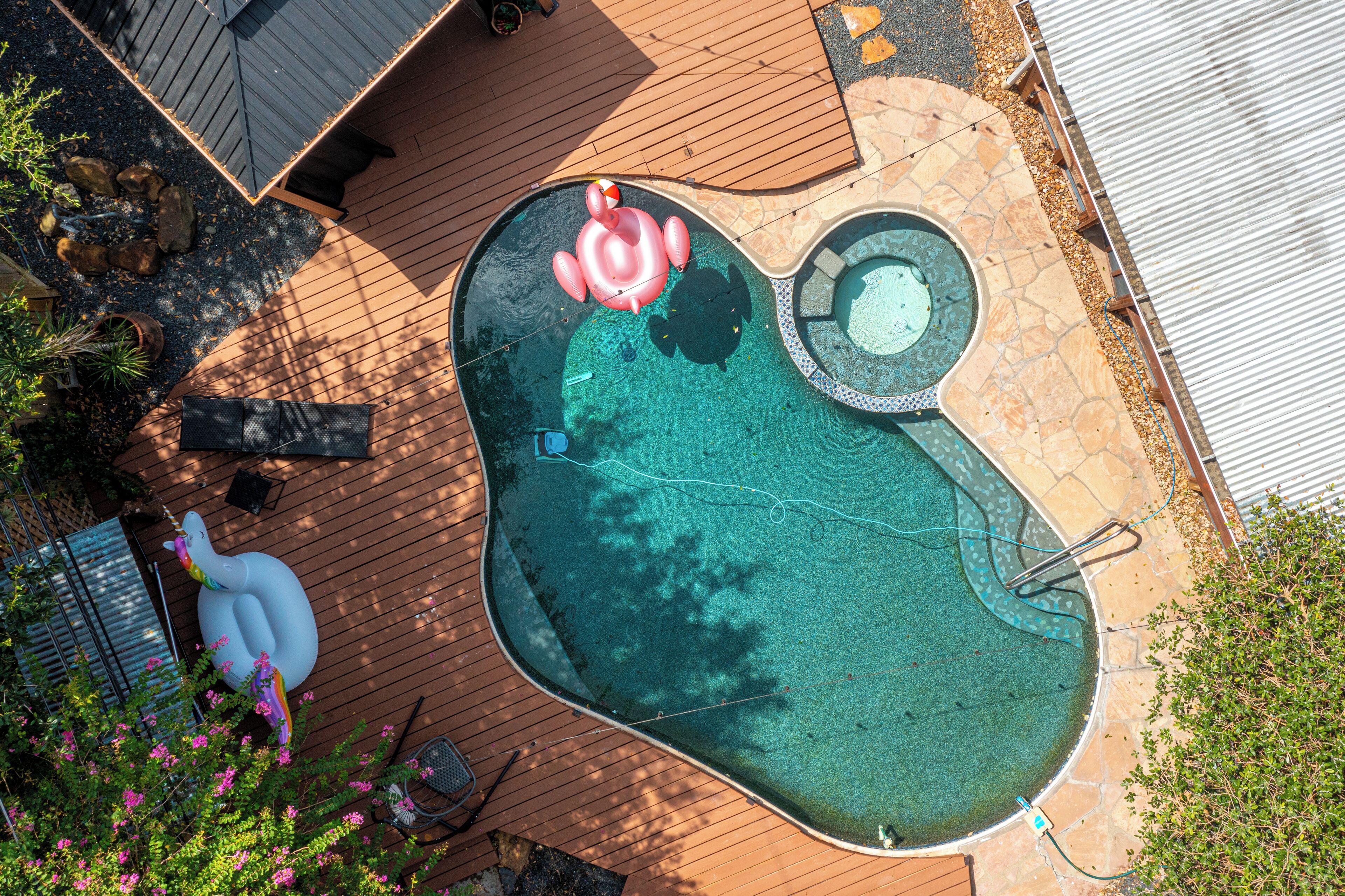 Een zwembad met een jacuzzi, omringd door een houten terras en potplanten.