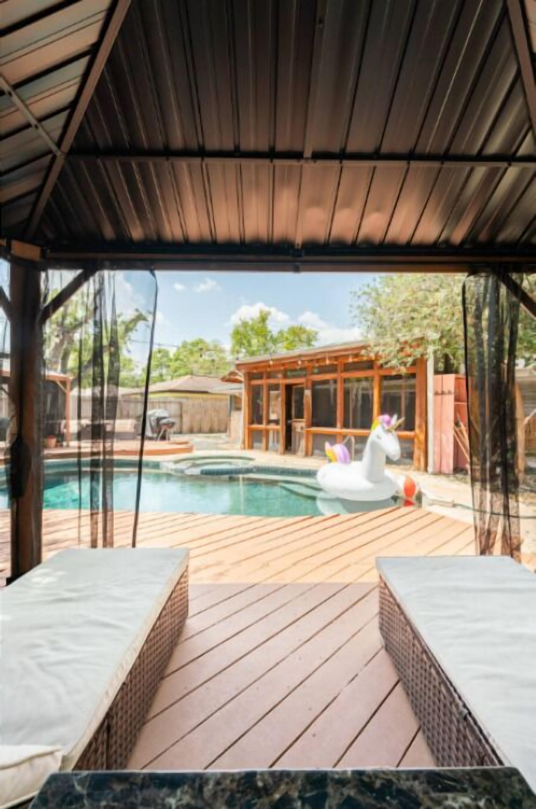 A covered outdoor swimming pool area with wooden decking, a hot tub, and a swan float.