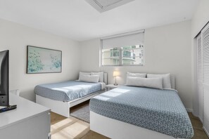 Une chambre moderne avec deux lits, un bureau, une télévision, une fenêtre et un tableau.