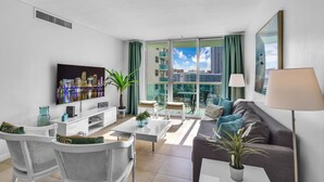 Un salon moderne doté d’un téléviseur à écran plat, d’un canapé, d’une table basse et d’un balcon offrant une vue sur la ville.