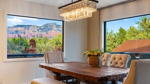 A dining area with a rustic wooden table, cushioned chairs, and a view of a mountain landscape through large windows. - Sedona At the Wild Horse, Wellness Retreat, Gameroom, Cold Plunge, West & Dry Sauna (Sedona)