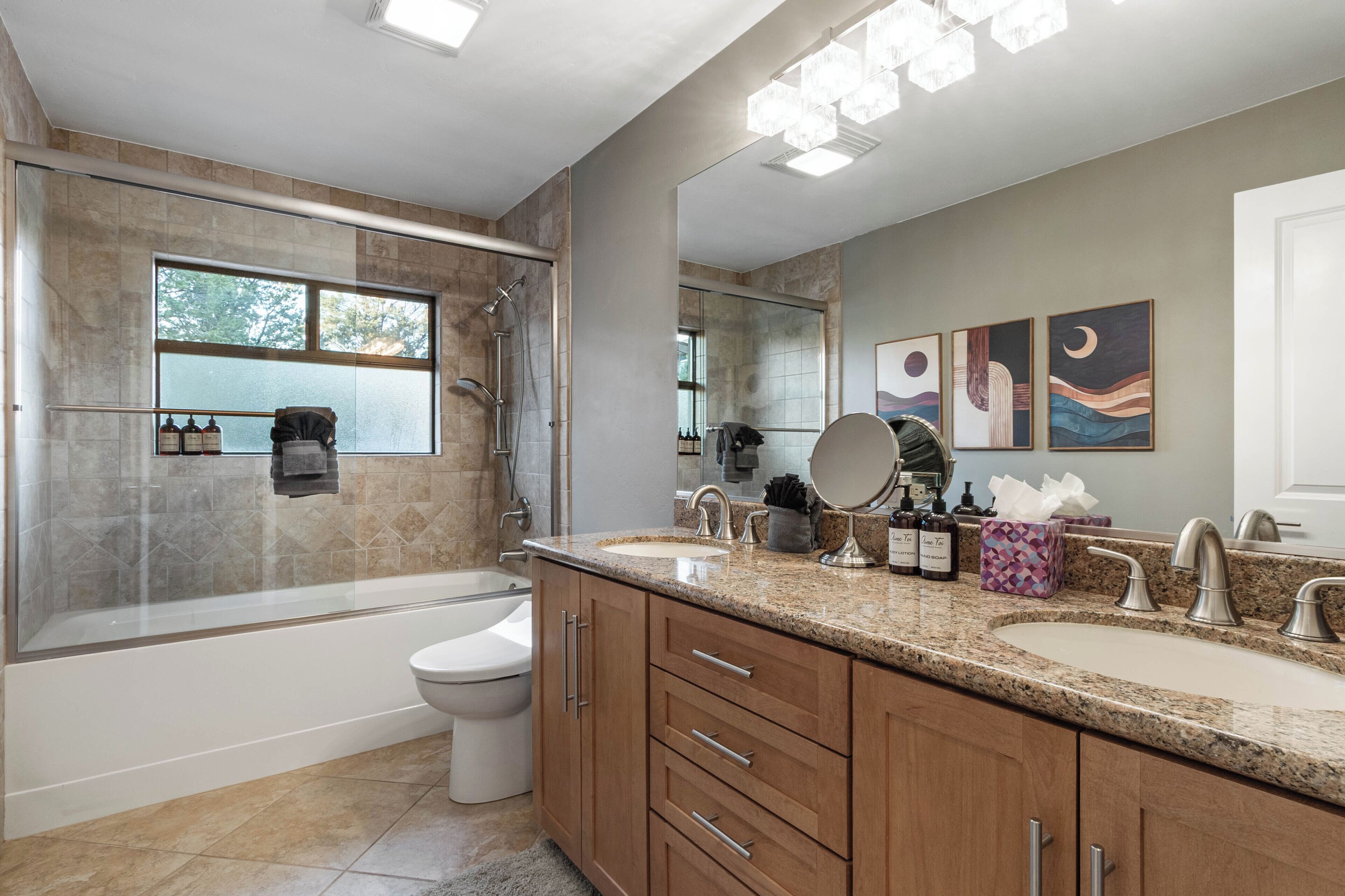 A modern bathroom with a bathtub, shower, and toilet. It features a large mirror, two sinks, and a vanity with drawers.