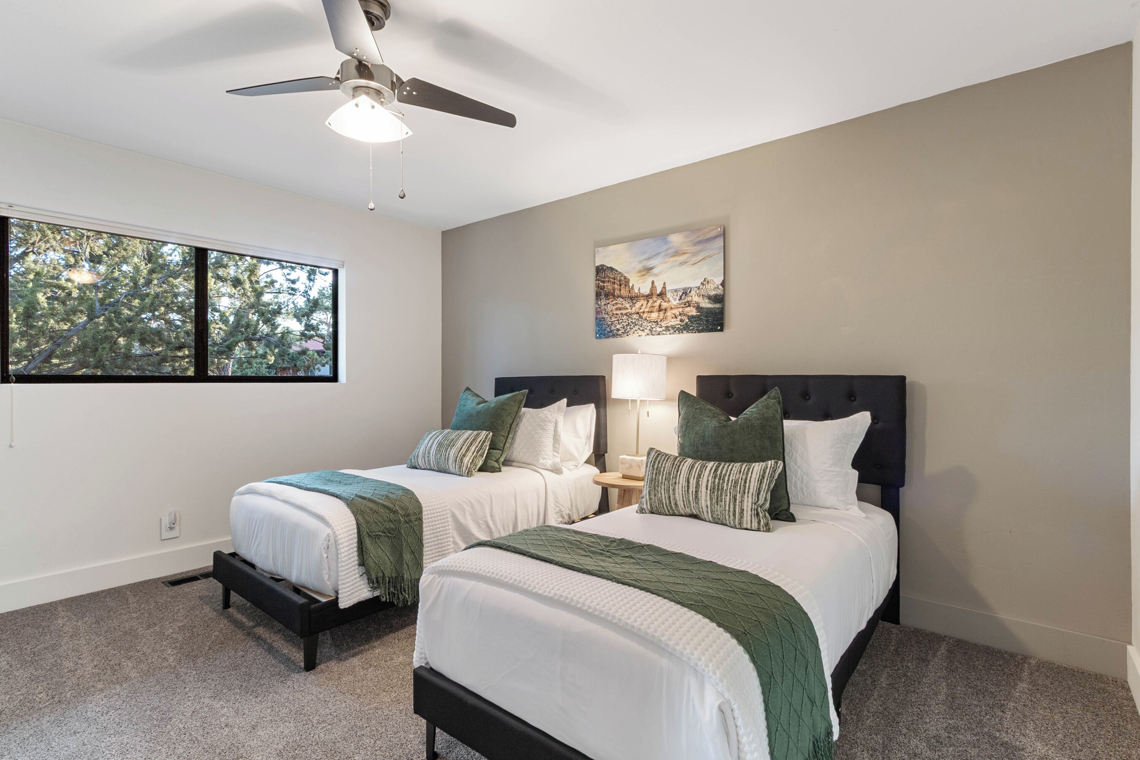 A bedroom with two beds, a ceiling fan, a painting, and a window.
