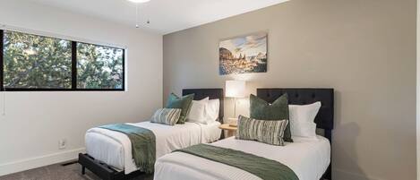 A bedroom with two beds, a ceiling fan, a painting, and a window.