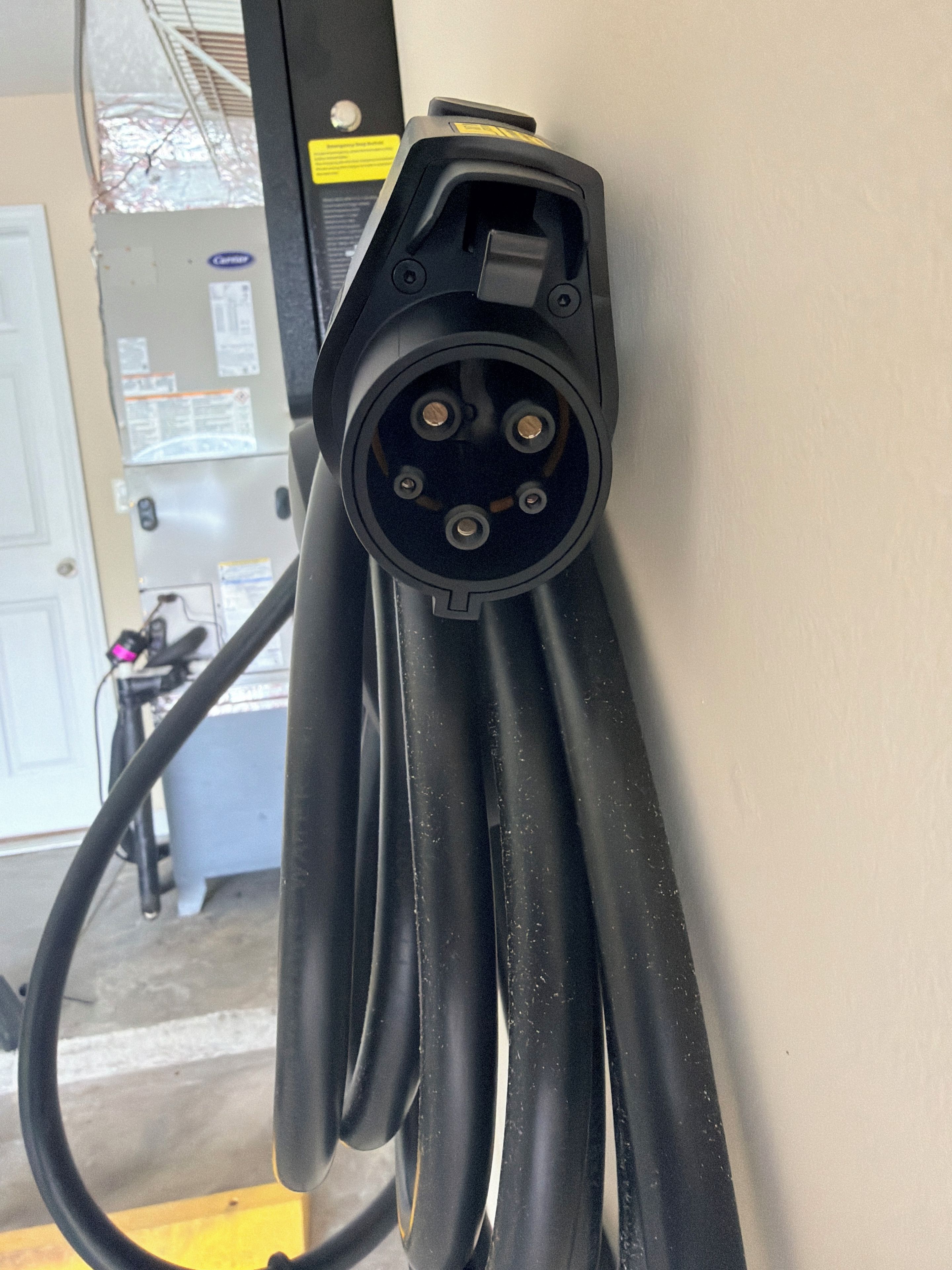 A close-up of a black electrical plug with multiple prongs, attached to a cable, against a wall.