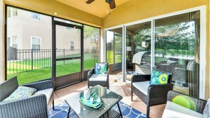 A covered patio with wicker furniture, a ceiling fan, and large sliding glass doors leading to a backyard.
