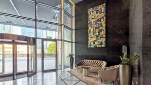 Een moderne lobby met een glazen ingang, een groot abstract schilderij, een stoffen bank en een potplant.