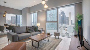 Een moderne woonkamer met een bank, salontafel en poef, grote ramen met uitzicht op de stad, en hanglampen.